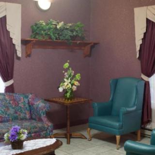 A cozy living room setting with a floral sofa, teal armchair, and decorative elements including curtains and potted plants.