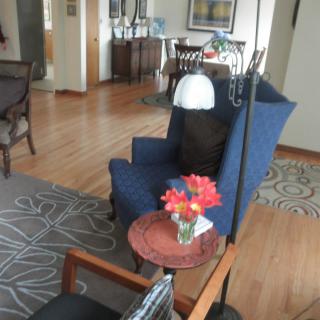A cozy living room with a blue chair, wooden floor, and a small table adorned with flowers.
