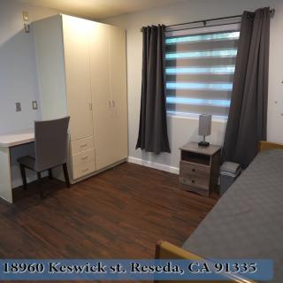 A tidy bedroom featuring a desk, chair, wardrobe, and a window with curtains.