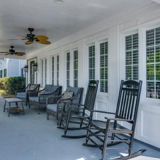 A spacious porch featuring rocking chairs and comfortable seating beneath ceiling fans, perfect for relaxation.