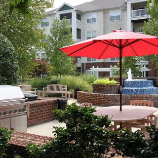 A peaceful outdoor patio with seating, a red umbrella, and a fountain at an apartment complex.
