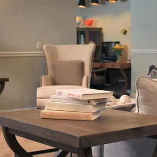 A cozy living room with a coffee table and armchair, featuring stacked books.