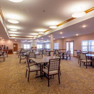 A spacious dining area with multiple tables and chairs, well-lit and featuring a carpeted floor.