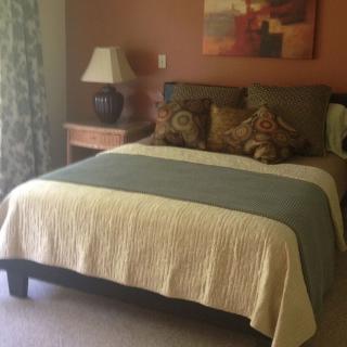 A cozy bedroom featuring a well-made bed with decorative pillows, a lamp on a wooden nightstand, and an abstract painting on the wall.