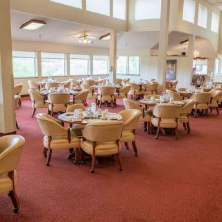 An elegant restaurant dining area with neatly arranged tables and chairs, featuring large windows and a carpeted floor.
