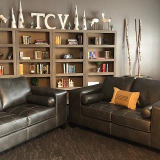 A cozy living room featuring two leather sofas, a bookshelf filled with books and decor, and a comfortable ambiance.
