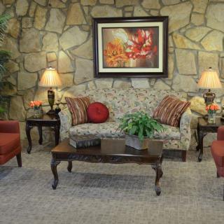 A cozy living room with a stone accent wall, featuring a floral sofa, red armchairs, a wooden coffee table, and decorative lamps.