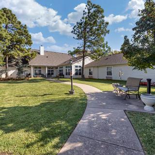 A spacious backyard with a pathway and outdoor furniture, surrounded by trees on a sunny day.