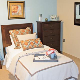 A cozy bedroom with a neatly made bed, decorative pillows, and a tray on the blanket.