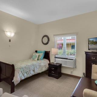 A cozy bedroom featuring a single bed beside a window, with a nightstand and a lamp.