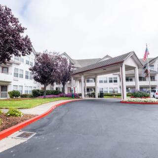 A spacious building entrance with a covered driveway and landscaped surroundings.