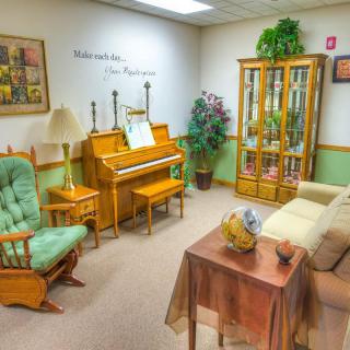 A cozy living room with a piano, rocking chair, and decorative cabinet.