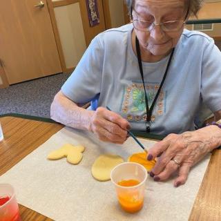 An elderly woman enjoying a painting activity indoors.