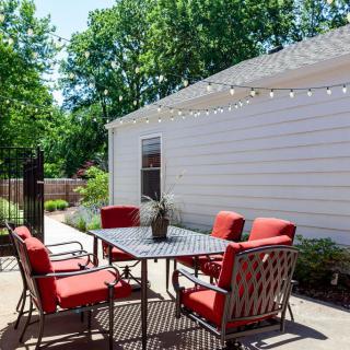 A cozy patio setup with red-cushioned chairs around a table, adorned with string lights in a sunny backyard setting.