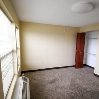 An empty room with carpet flooring, a window allowing natural light, and a wooden wardrobe.