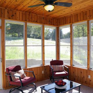 A cozy sunroom with wood paneling, featuring comfortable seating and abundant natural light.