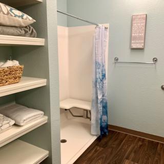 A bathroom featuring a shower with a blue and white curtain, adjacent shelves stocked with towels and a basket.