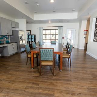 A spacious dining room with a large wooden table and chairs, featuring a modern kitchen area and wooden flooring.