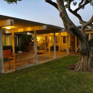 A cozy evening view of a well-lit home surrounded by landscaping and trees.