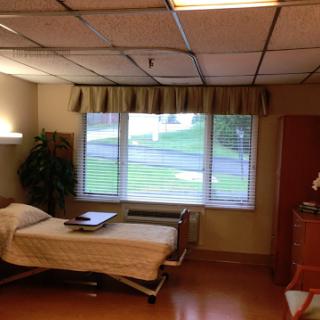 A well-lit hospital room featuring a bed, window with curtains, and a small plant.