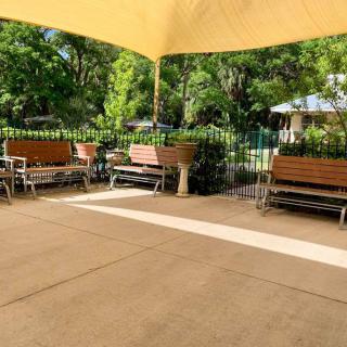 A peaceful outdoor patio with benches under a shade canopy surrounded by lush greenery.