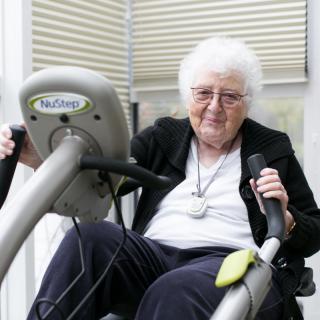 An elderly woman exercising on fitness equipment indoors, highlighting an active lifestyle.
