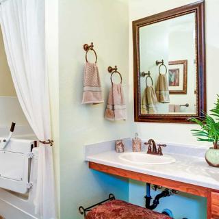 A well-decorated bathroom featuring a sink with a mirror above, towels hanging on rings, a potted plant, and a shower area with a curtain.