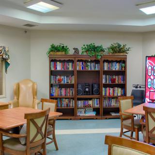 A cozy reading room with bookshelves, tables, and chairs, decorated with plants.