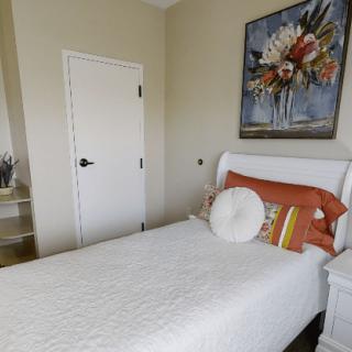 A cozy bedroom with a single bed, decorative pillows, and a floral painting on the wall.