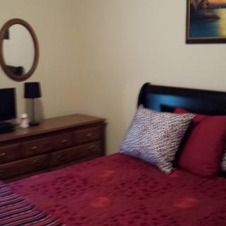 A cozy bedroom with a red-themed bedding set, wooden dresser, and mirror.
