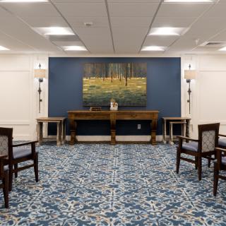 A well-lit room with a patterned carpet and neatly arranged chairs, featuring a painting on the wall.