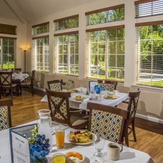 A cozy dining room with sunlit windows, set for a breakfast meal.