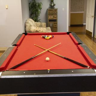 A red-felted pool table with crossed pool cues and a rack of billiard balls in a recreation room.
