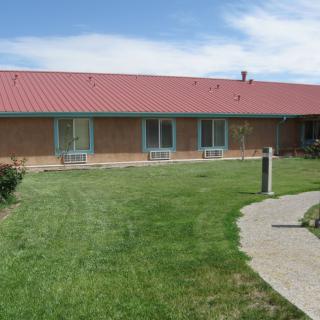 A single-story building with a red roof, surrounded by a green lawn and concrete pathway under a blue sky.