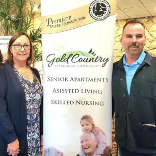 Two individuals standing next to a banner for Gold Country senior living services.