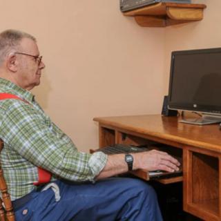 An elderly man sits at a desk typing on a computer.