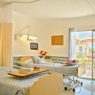A well-lit hospital room featuring a patient bed and medical equipment, with a window offering an outdoor view.