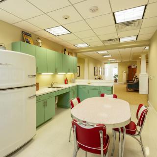 A retro-style kitchen with pastel green cabinets, a vintage refrigerator, and a dining table with red chairs.
