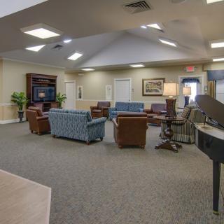 A spacious living room area with assorted furniture, including sofas, chairs, a piano, and a television.