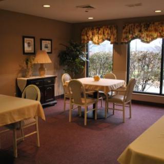A cozy dining room with neatly arranged tables and chairs, soft lighting, and large windows offering a view outside.