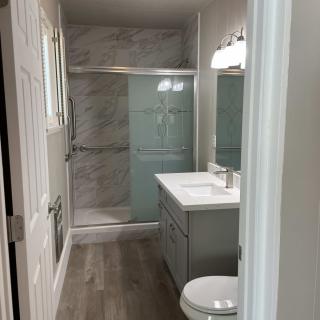A modern bathroom with a shower, sink, and toilet featuring tile walls and wooden flooring.