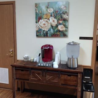 A cozy refreshment station with a coffee machine, water dispenser, and floral artwork.