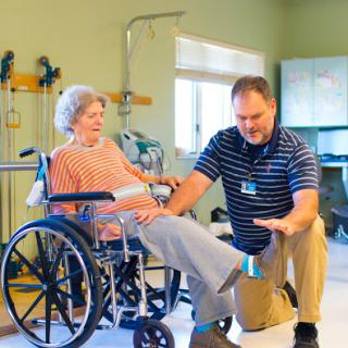 A therapist is assisting an elderly patient in a wheelchair during a physical therapy session.