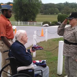 A veteran in a wheelchair receives honors from a service member during a ceremony.