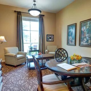 A cozy living room with elegant furniture and decor, featuring a table, armchair, sofa, and large window.