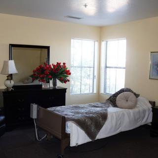 A cozy bedroom with a single bed, dresser with flowers, and a lamp by the window.