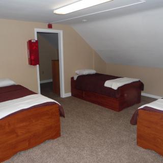 A simple attic bedroom with three single beds and a carpeted floor.