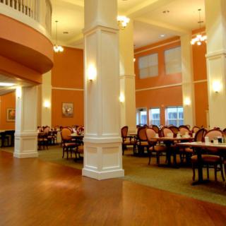 An elegant dining area featuring neatly arranged tables and chairs, with warm lighting and high ceilings.