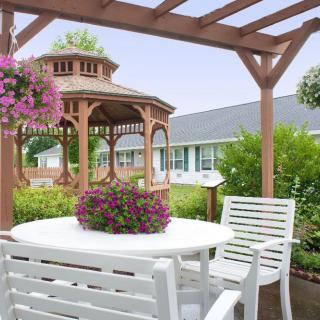 A serene garden setting with a gazebo, pergola, and white patio furniture surrounded by vibrant flowers.