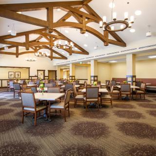 A spacious dining area with multiple tables and chairs, adorned with chandeliers and wooden beams.